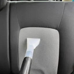 Dysza odkurzacza piorącego na szarym, materiałowym siedzeniu samochodowym podczas czyszczenia.