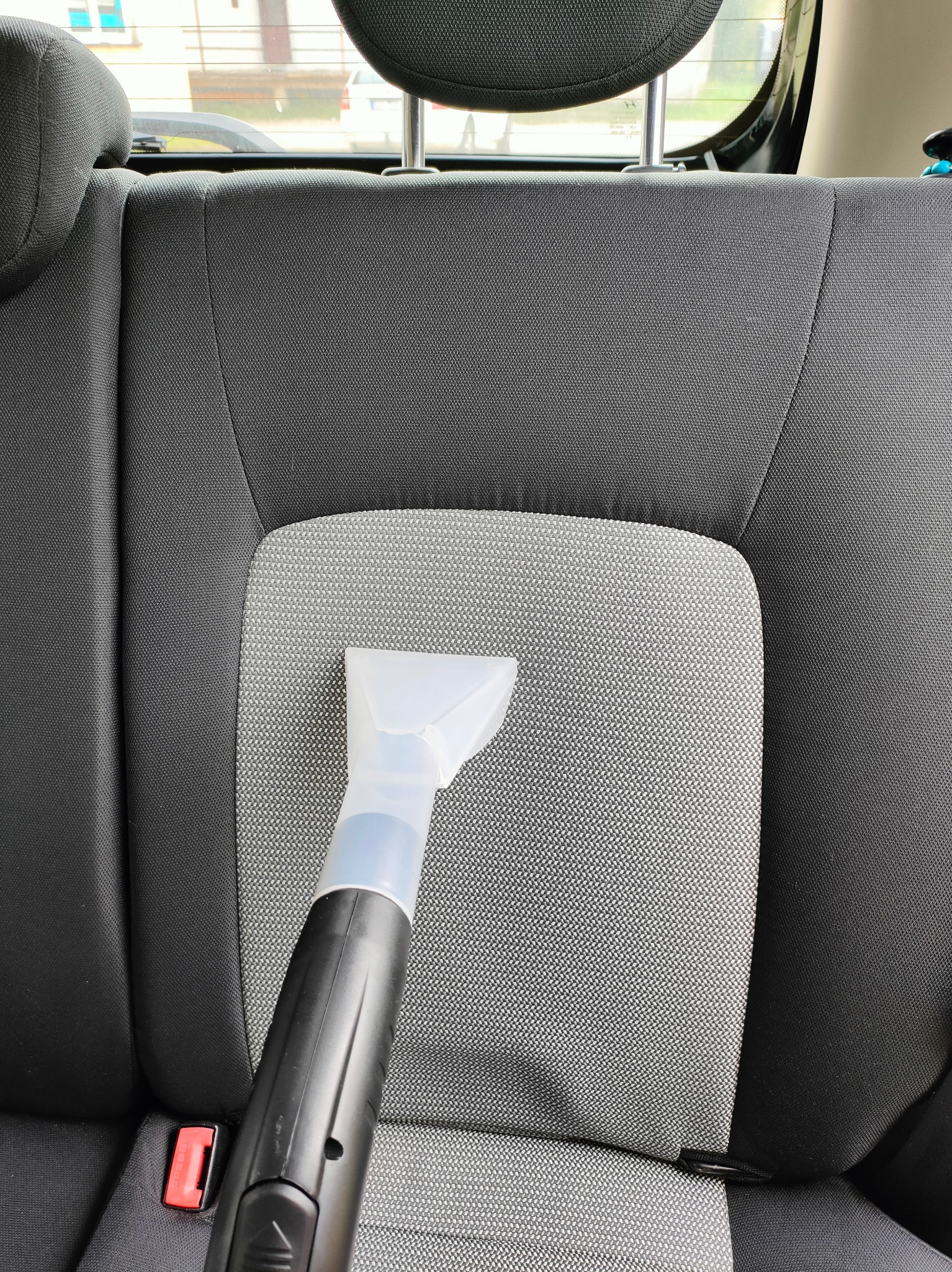 Dysza odkurzacza piorącego na szarym, materiałowym siedzeniu samochodowym podczas czyszczenia.