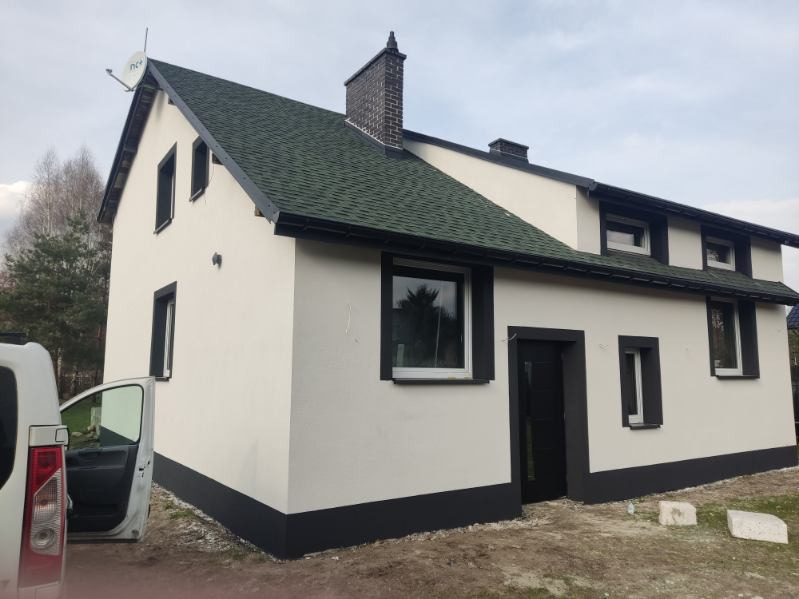 Dom w Katowicach z jasną elewacją wykończoną ciemnymi detalami, widoczny samochód z otwartymi drzwiami i zielony dach z satelitą.