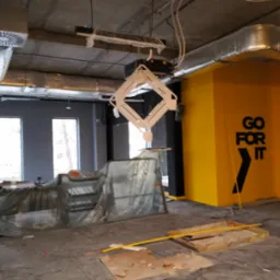 Siłownia w trakcie prac: widoczne elementy instalacji pod sufitem, żółta ściana z napisem 'GO FOR IT', podłoga zabezpieczona folią. Etap prac w aquaparku.