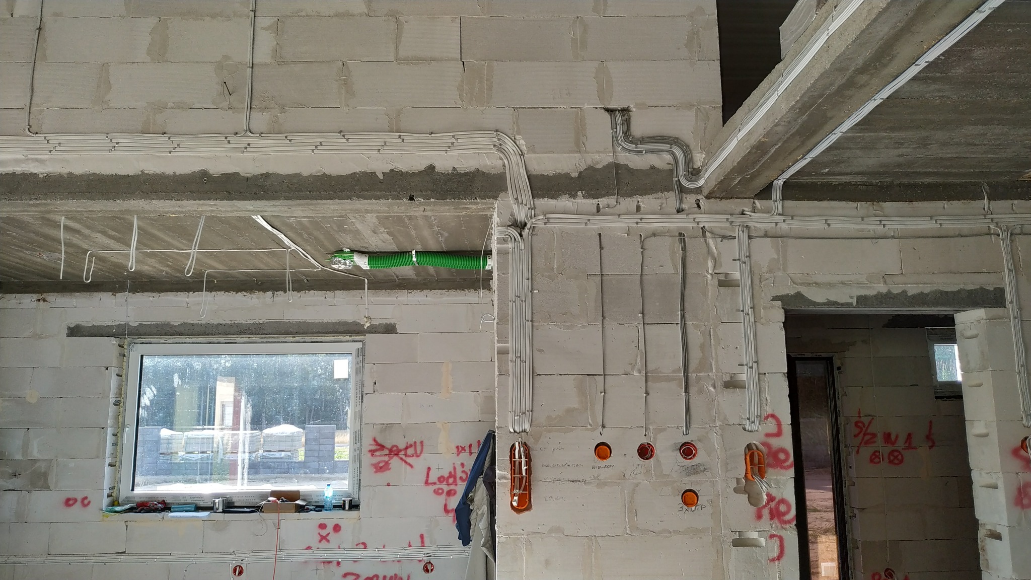 Surowe wnętrze w trakcie prac: widoczne kable elektryczne prowadzone po ścianach z betonu komórkowego, puszki instalacyjne i fragment wentylacji w zielonej rurze karbowanej.