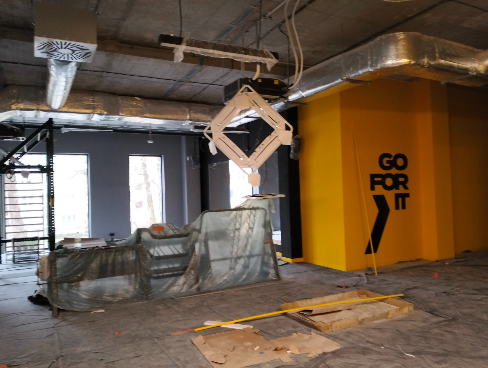 Siłownia w trakcie prac: widoczne elementy instalacji pod sufitem, żółta ściana z napisem 'GO FOR IT', podłoga zabezpieczona folią. Etap prac w aquaparku.