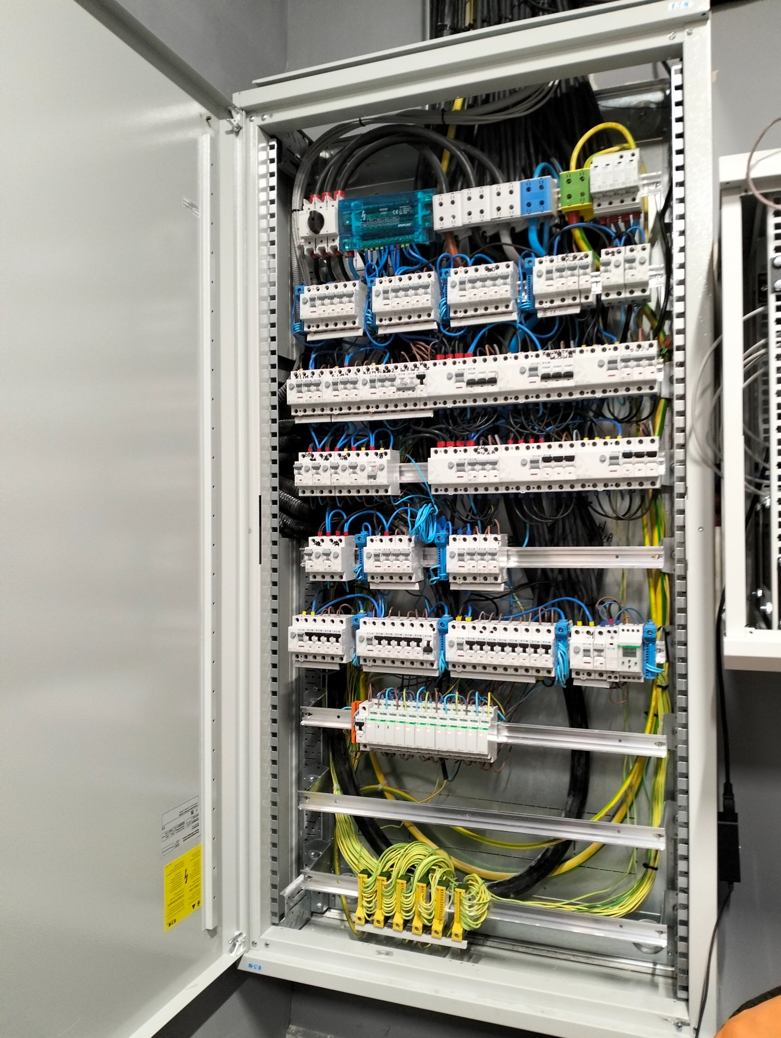 Otwarta szafa sterownicza z precyzyjnie ułożonymi przewodami i zabezpieczeniami, widoczne detale instalacji elektrycznej w obiekcie komercyjnym.