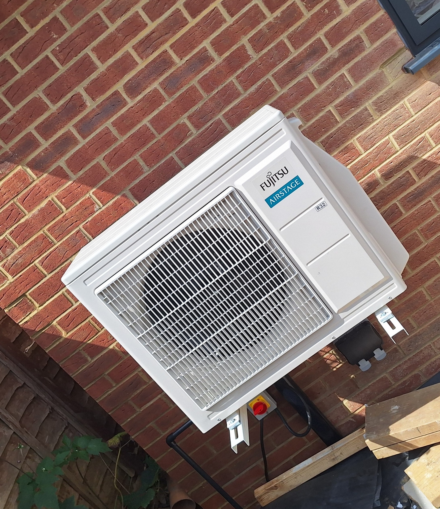 Zewnętrzna jednostka klimatyzacji Fujitsu Airstage R32 zamontowana na ceglanej ścianie budynku, widoczny przewód elektryczny i fragment instalacji.