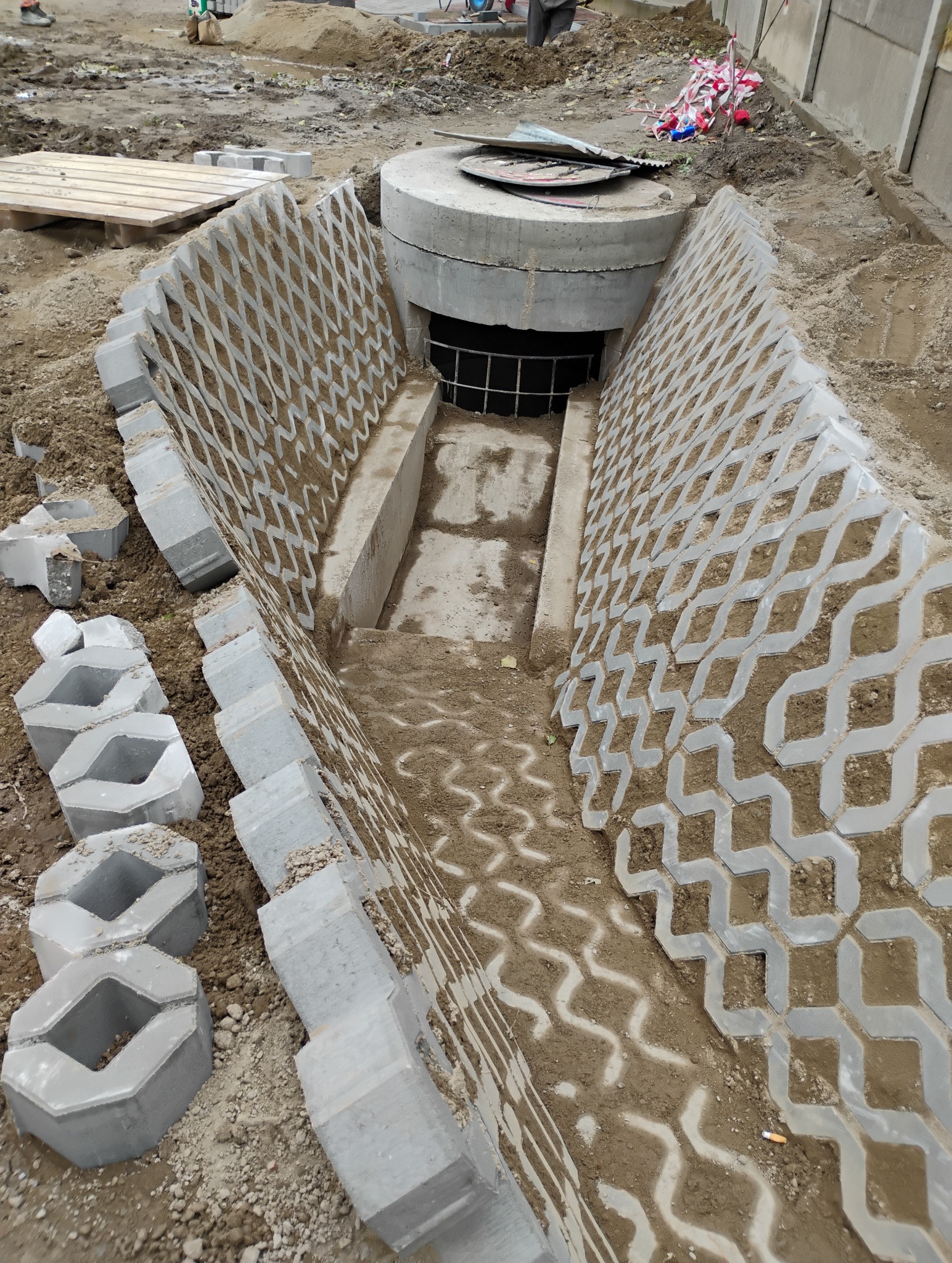 Budowa studzienki kanalizacyjnej z użyciem ażurowych betonowych elementów, widoczne ułożone ściany i przygotowane do montażu kolejne bloczki.