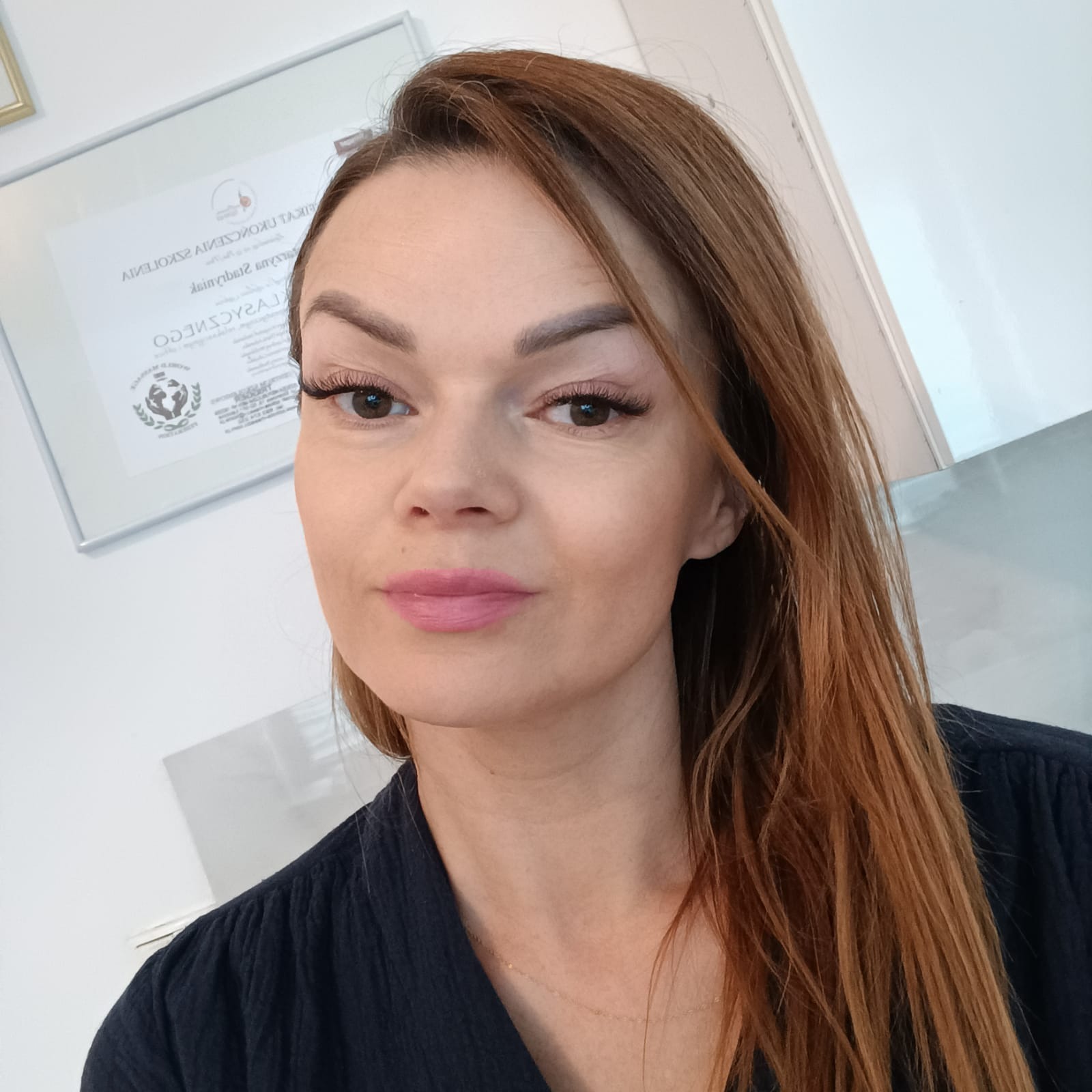 Portret kobiety z przedłużonymi rzęsami, delikatnym makijażem i certyfikatem w tle.