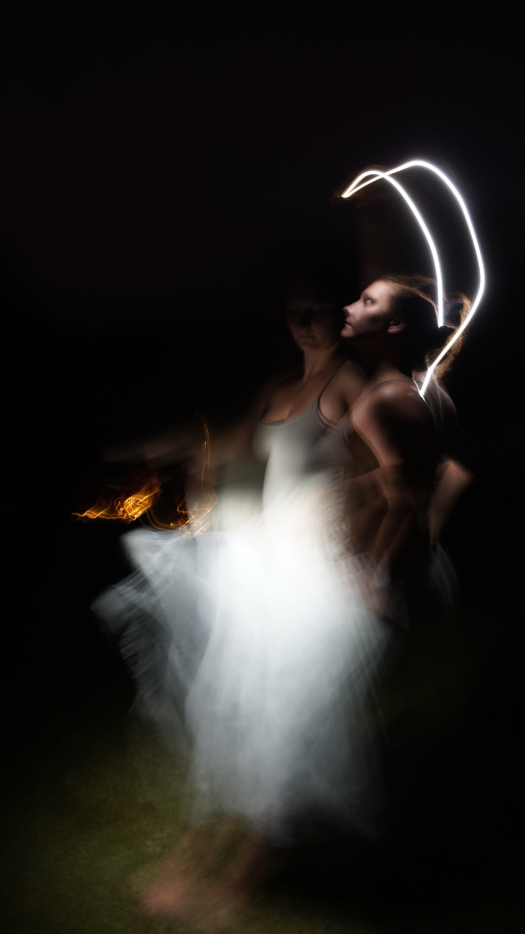 Dwie kobiety w ruchu, jedna trzymająca płonący obiekt, druga z jasnymi liniami wokół głowy w ciemnym otoczeniu, efekt rozmycia ruchu.
