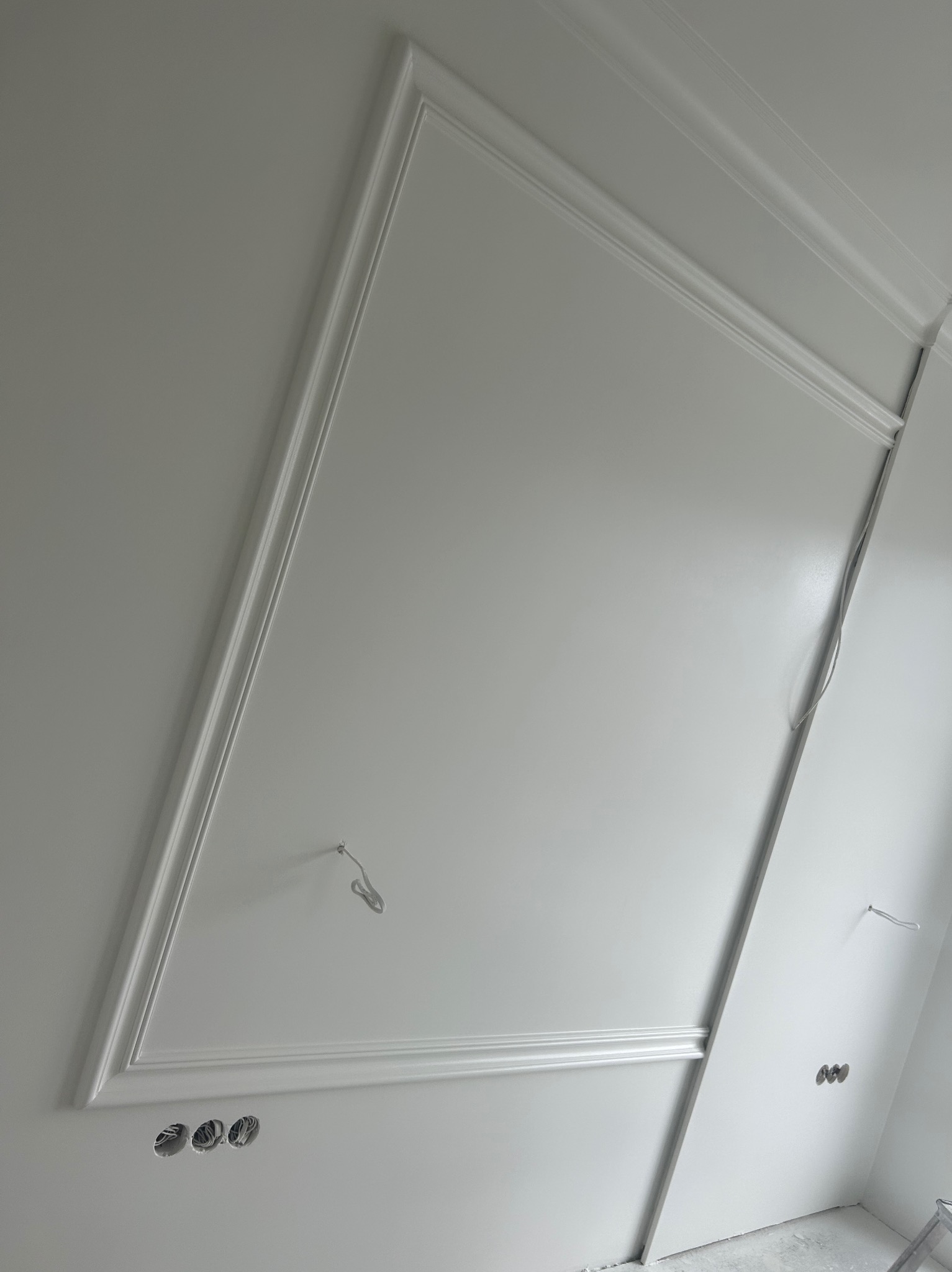 Ściana z listwami dekoracyjnymi i przygotowanymi otworami na gniazdka elektryczne, widoczne przewody, surowy stan wykończenia.