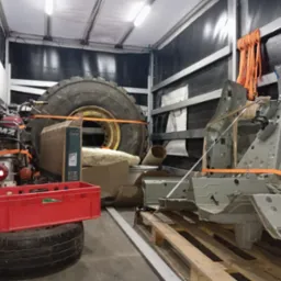 Wnętrze przestrzeni ładunkowej z zabezpieczonym ładunkiem: opona od traktora, motocykl MZ, karoseria samochodu i inne przedmioty, wszystko spięte pomarańczowymi pasami.