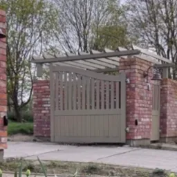 Brama wjazdowa z ceglanymi słupkami i drewnianą pergolą, oświetlona lampą w stylu retro, prowadząca na posesję.