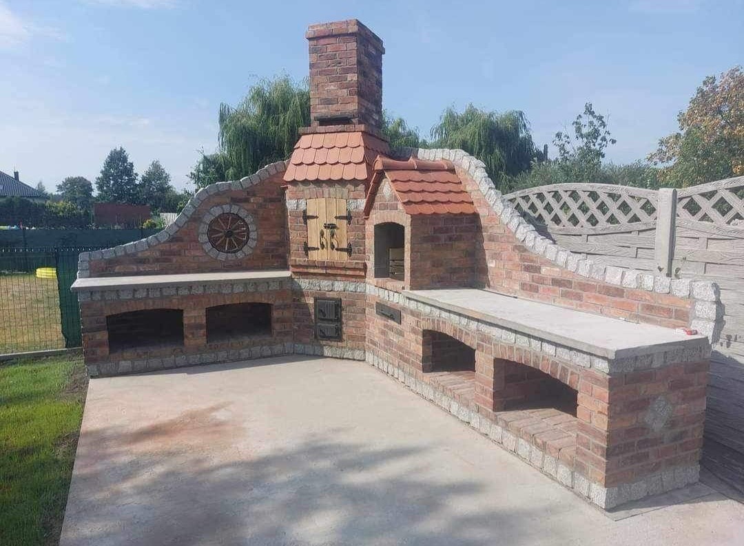 Zewnętrzny, murowany grill z cegły z wędzarnią i blatem roboczym, wykończony elementami dekoracyjnymi z drewna i kamienia, na betonowym podłożu.