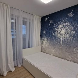 Santi Łukasz Burkiewicz - Pokój z łóżkiem jednoosobowym, ścianą z motywem dmuchawca i białymi zasłonami.