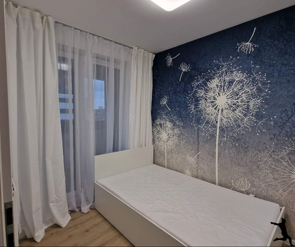Pokój z łóżkiem jednoosobowym, ścianą z motywem dmuchawca i białymi zasłonami.