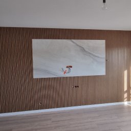 Voitech Studio - Pusty pokój z drewnianą ścianą z listew, na której wisi płyta imitująca marmur z wystającymi kablami elektrycznymi, szare ściany boczne i jasna podłoga.