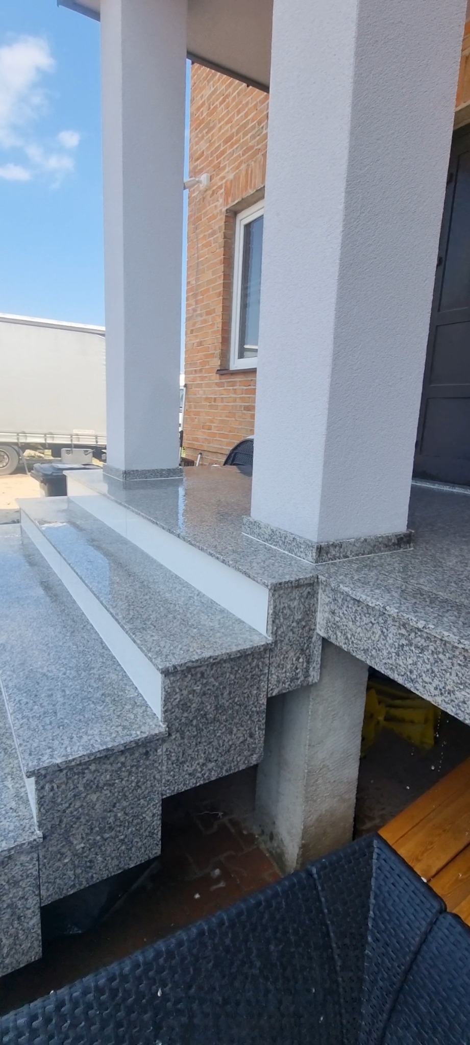 Zewnętrzne schody wejściowe wyłożone płytami granitowymi w odcieniach szarości, z białymi akcentami na krawędziach stopni i cokołach kolumn, prowadzące do wejścia z kolumnami o fakturze baranka...