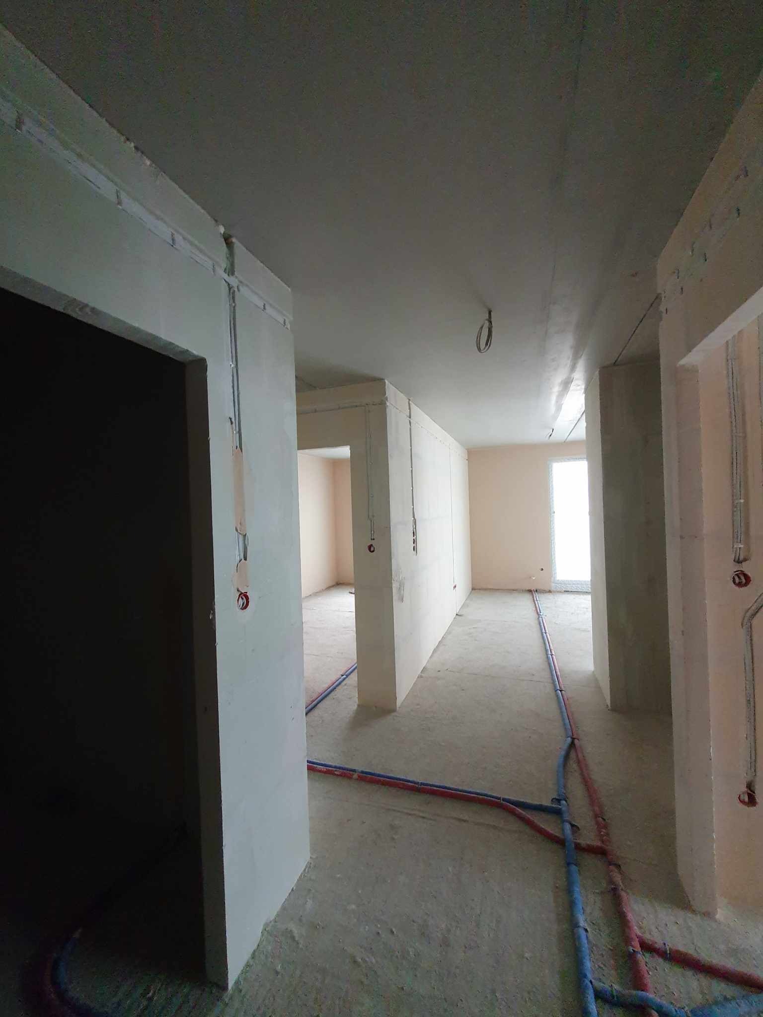 Wnętrze w trakcie remontu: widoczne kable elektryczne i rury instalacji wodnej prowadzone po podłodze i ścianach w surowym stanie.