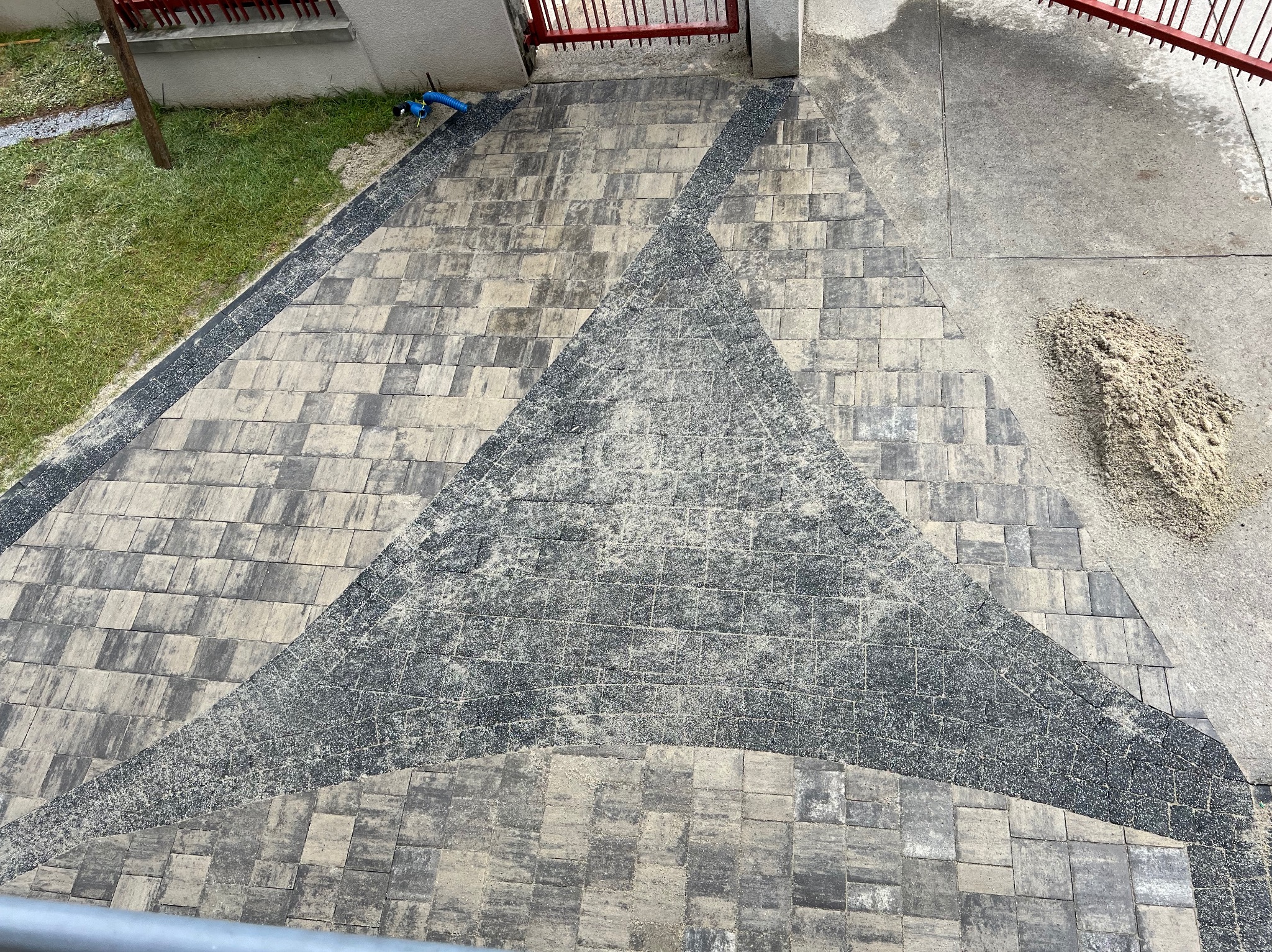 Ułożona kostka brukowa w szarościach z geometrycznym wzorem trójkąta, widok z góry, z pozostałościami piasku na powierzchni.