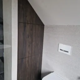 Szafka wnękowa z ciemnego drewna w łazience ze spłuczką podtynkową i toaletą wiszącą.