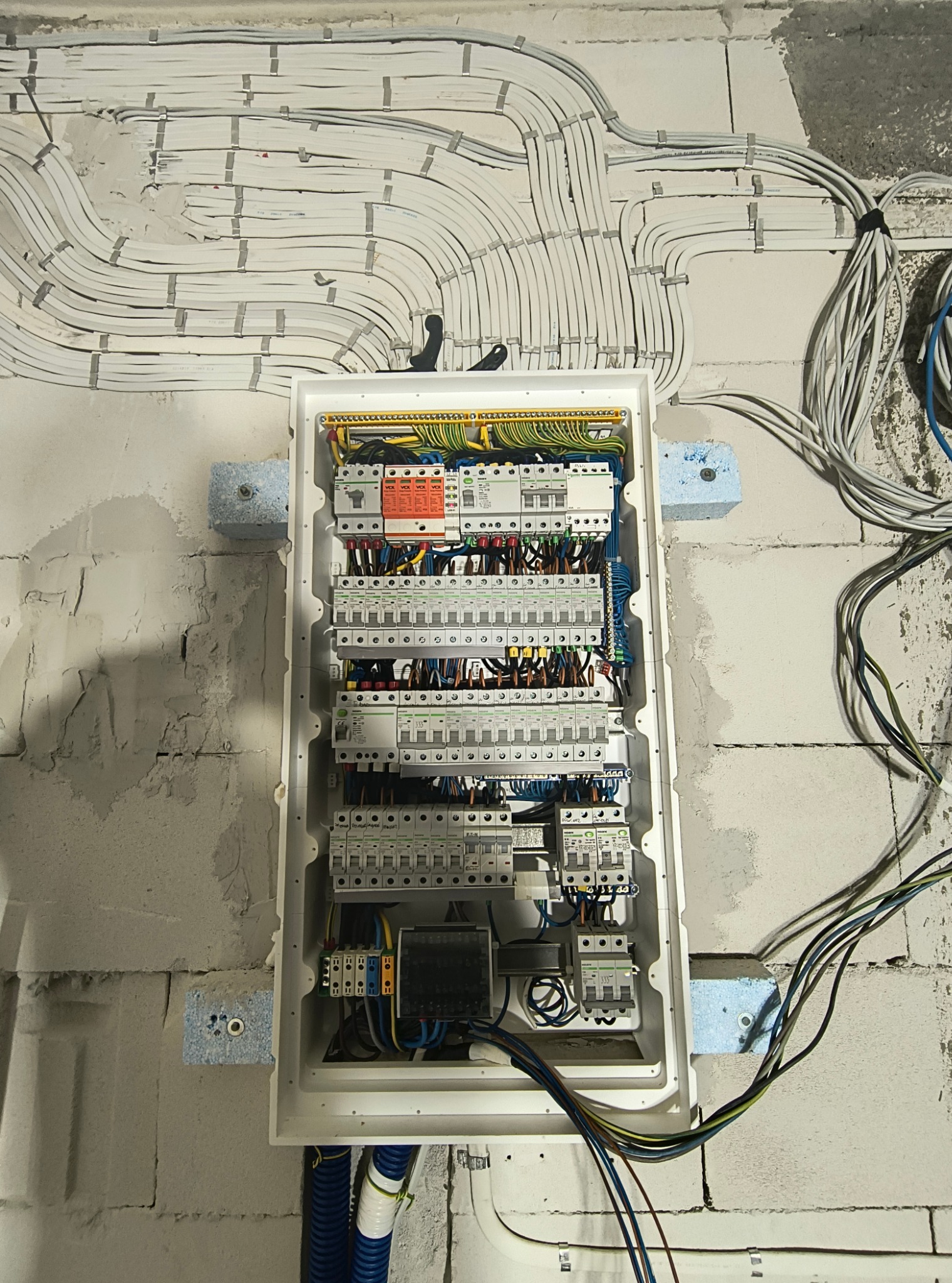 Rozdzielnia elektryczna w trakcie montażu na ścianie z bloczków. Widoczne kable prowadzone po ścianie i wchodzące do rozdzielni.