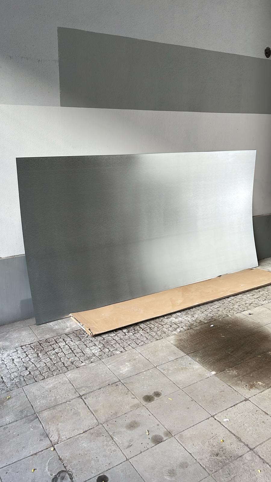 Płyta aluminiowa oparta o ścianę na chodniku z kostki, zabezpieczona kartonem