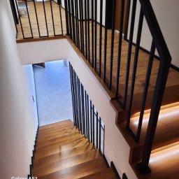Steel Creative Mateusz Bartczak - Wewnętrzne schody drewniane z podświetleniem LED i czarną, prostą balustradą metalową, widok z góry.