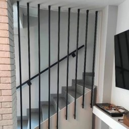 Steel Creative Mateusz Bartczak - Nowoczesne schody z czarnymi, pionowymi słupkami i poręczą, ściana z białej cegły, widok z dołu na górę.