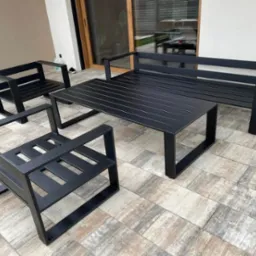 Czarny, minimalistyczny zestaw mebli ogrodowych ze stali: sofa, dwa fotele i stół, ustawiony na płytkach tarasowych, widok z boku.