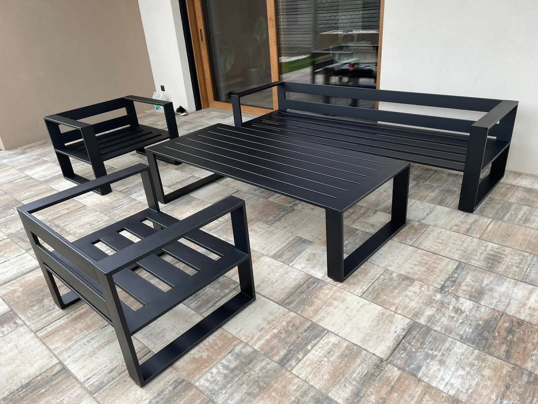 Czarny, minimalistyczny zestaw mebli ogrodowych ze stali: sofa, dwa fotele i stół, ustawiony na płytkach tarasowych, widok z boku.