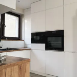 Nowoczesna kuchnia z białymi, lakierowanymi frontami, drewnianym blatem przy zlewie i zabudowanymi piekarnikami marki Electrolux.