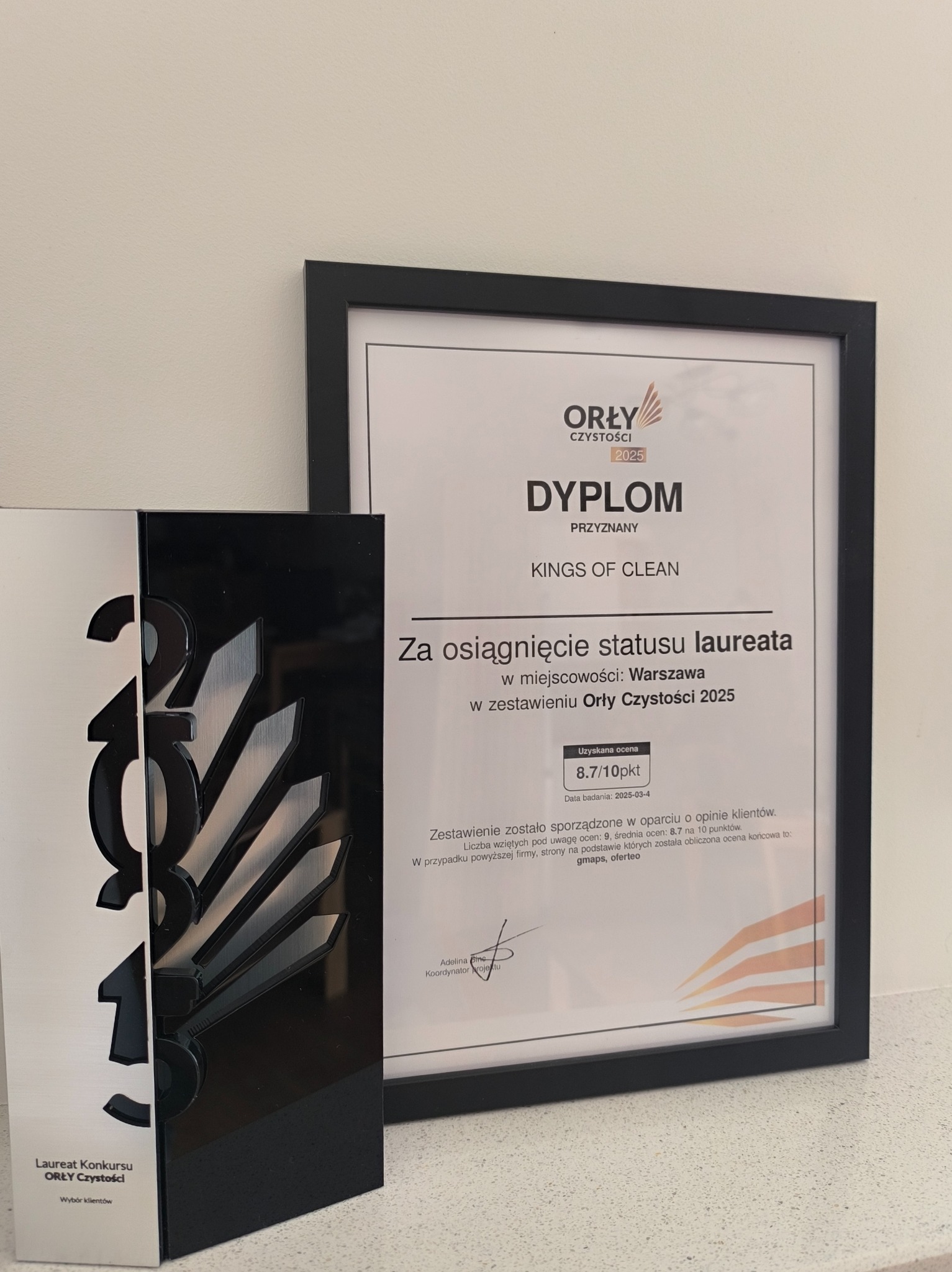 Dyplom Orły Czystości 2025 w czarnej ramce, obok statuetka Laureata Konkursu Orły Czystości z napisem Wybór Klientów. Dyplom przyznany dla Kings of Clean za osiągnięcie statusu laureata w Warszawie...