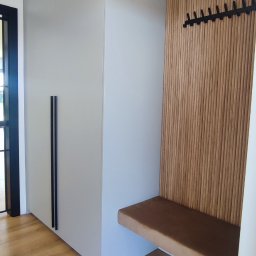 Meblopolis - Szara szafa w przedpokoju z czarnymi uchwytami, drewniany panel ścienny z wieszakami i siedziskiem w kolorze brązowym, na podłodze panele imitujące drewno.
