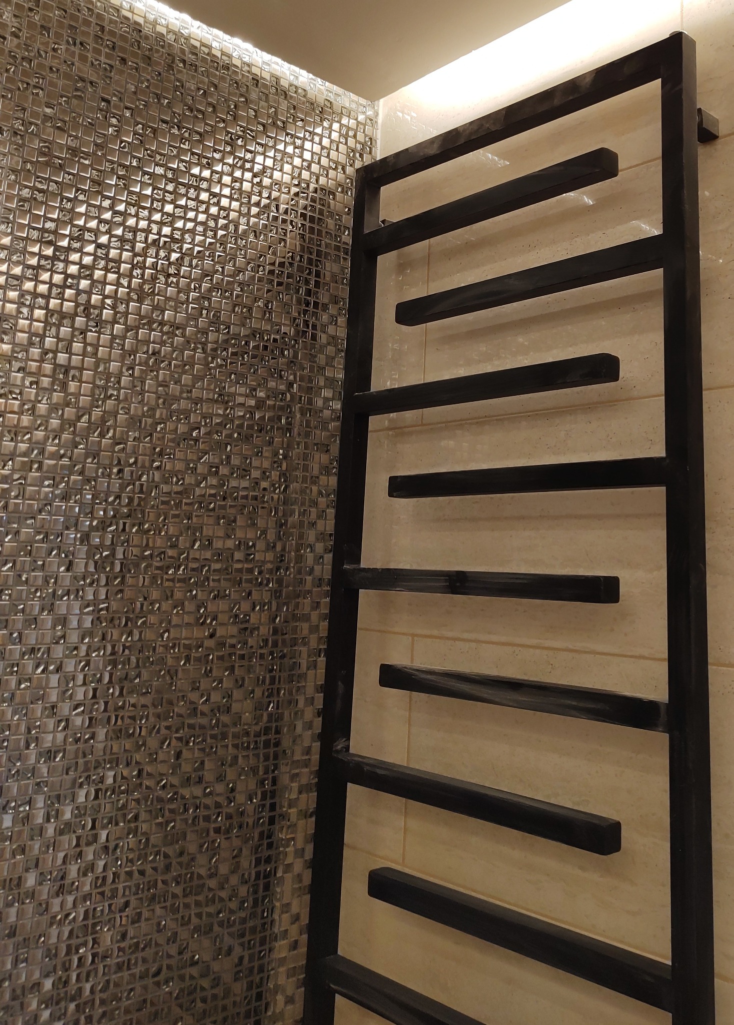 Nowoczesna łazienka z błyszczącą mozaiką na ścianie i czarnym, drabinkowym grzejnikiem.