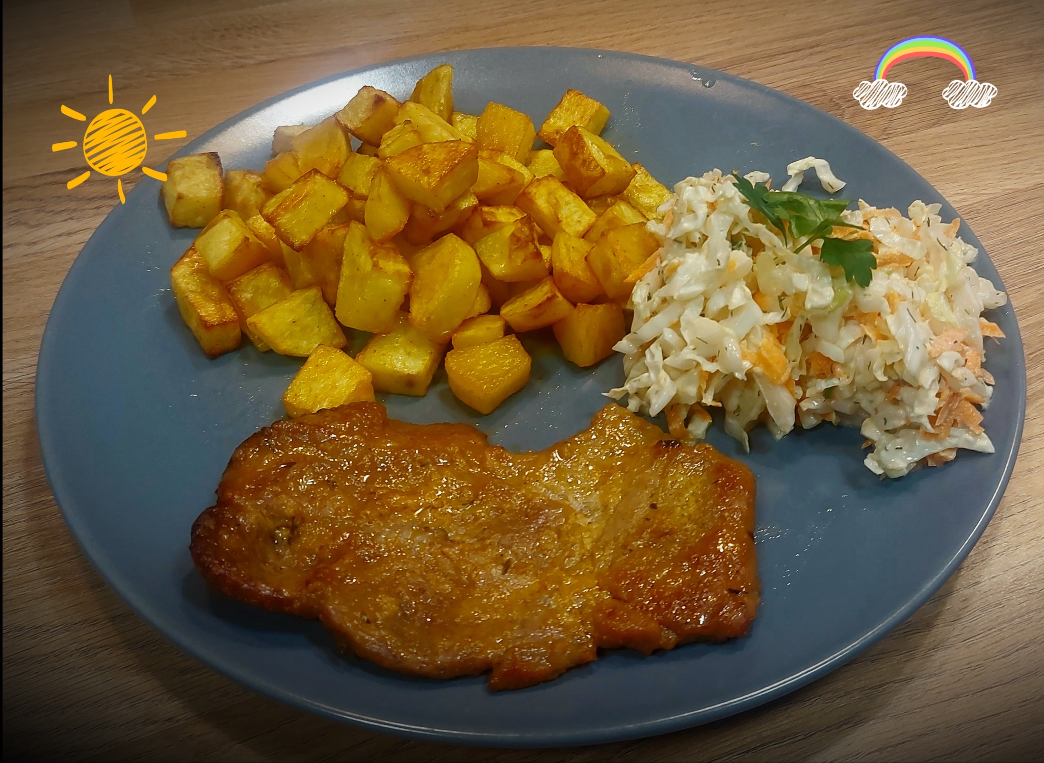 Gotowy obiad na szarym talerzu: kotlet w panierce z sosem, smażone ziemniaki w kostkę i surówka colesław z zieloną pietruszką, ozdobiony naklejkami słońca i tęczy.