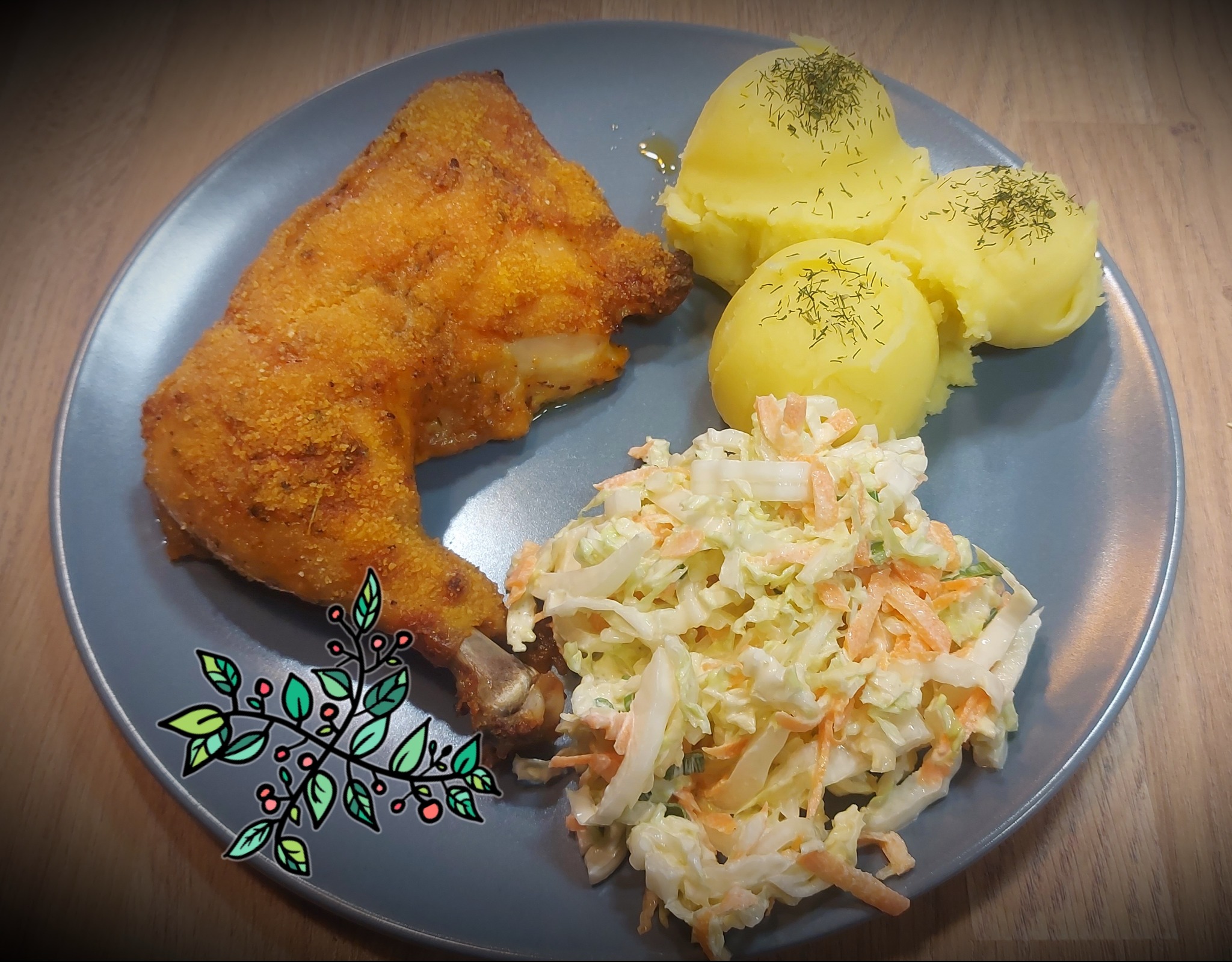 Porcja obiadowa na szarym talerzu: panierowana noga kurczaka, trzy kulki ziemniaczanego puree posypane koperkiem i surówka colesław z marchewką.