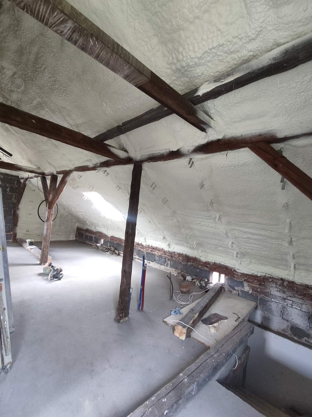 Poddasze po izolacji natryskowej, widoczne drewniane belki konstrukcyjne i nierówna powierzchnia izolacji.