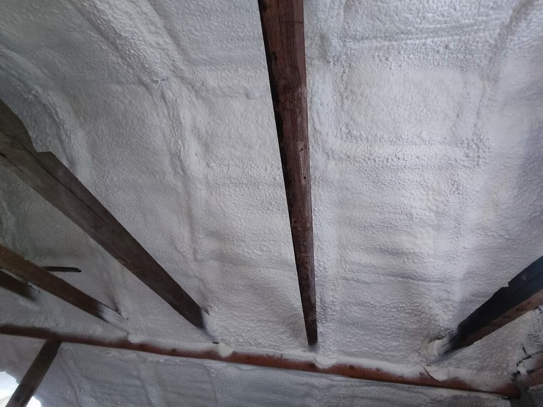 Strop poddasza ocieplony białą pianą izolacyjną, widoczne drewniane belki konstrukcyjne.