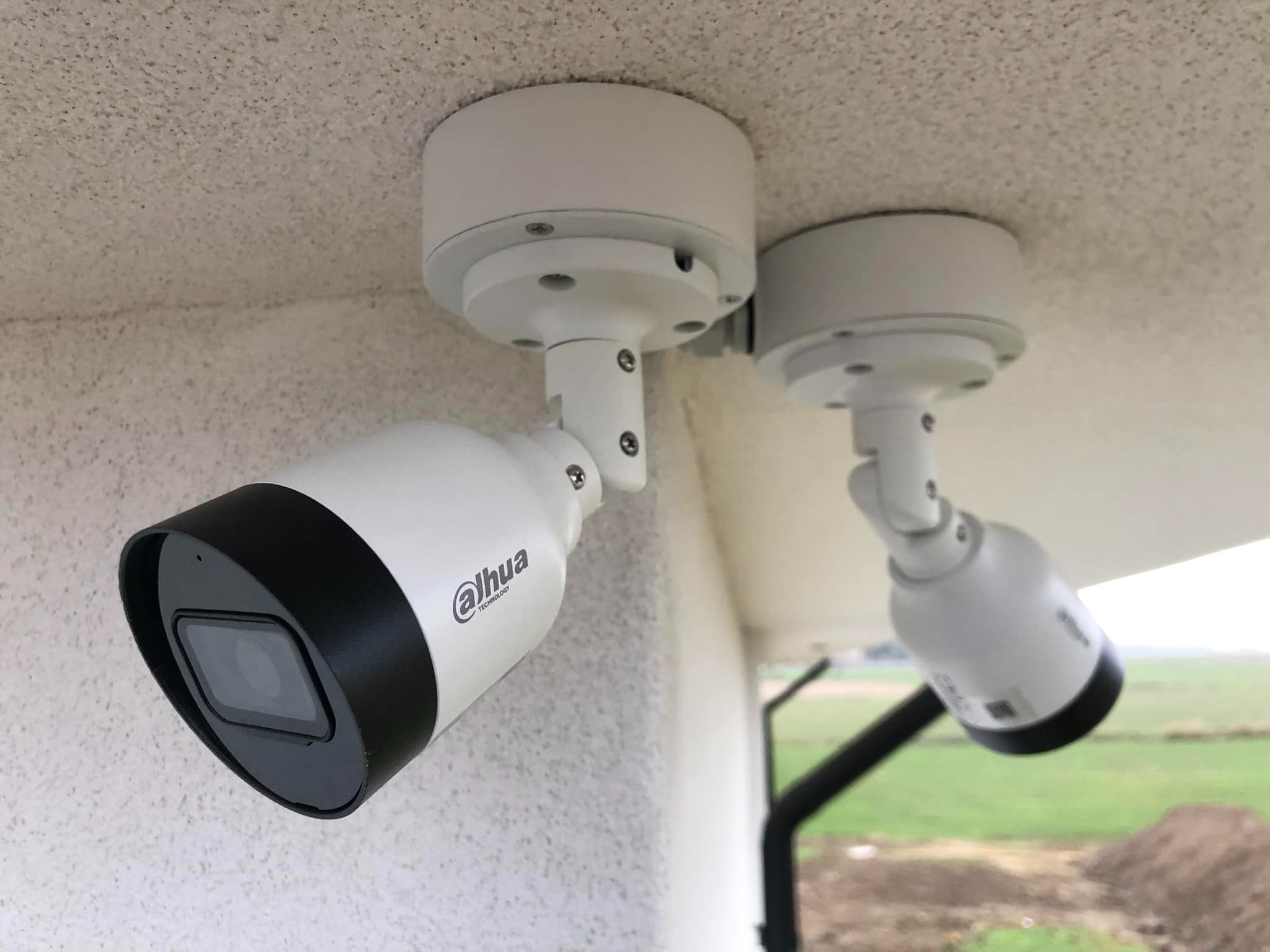 Dwie kamery monitoringu Dahua zamontowane pod sufitem, skierowane w różnych kierunkach. Widoczne mocowania i fragment otoczenia zewnętrznego.