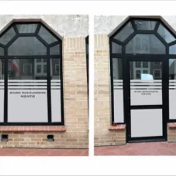 Fasada budynku z oknem i drzwiami wejściowymi, na szybach naklejki z napisem 'BIURO RACHUNKOWE KONTO'.