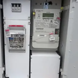 Zamknięta skrzynka z zamontowanymi licznikami energii elektrycznej i zabezpieczeniami. Widoczne plombowania i etykiety identyfikacyjne.