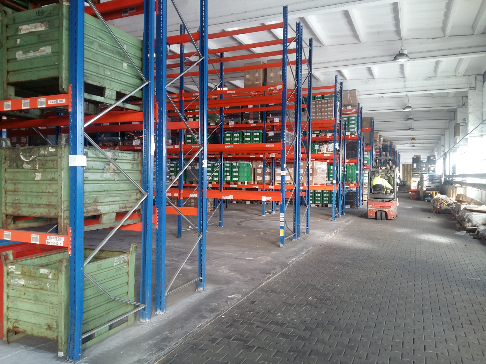 Wnętrze magazynu z regałami wypełnionymi towarami, widoczny wózek widłowy w oddali.