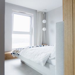Noglik Photo - Jasna sypialnia z dużym oknem, białymi ścianami i podłogą, minimalistycznym łóżkiem z białą pościelą i wzorzystą narzutą, oraz wiszącymi kulistymi lampami.