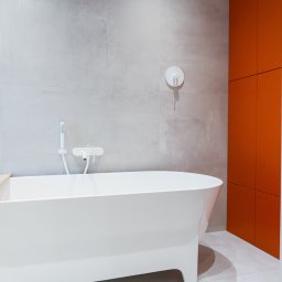 Noglik Photo - Minimalistyczna łazienka z wolnostojącą białą wanną, szarą ścianą z armaturą i pomarańczową szafką.