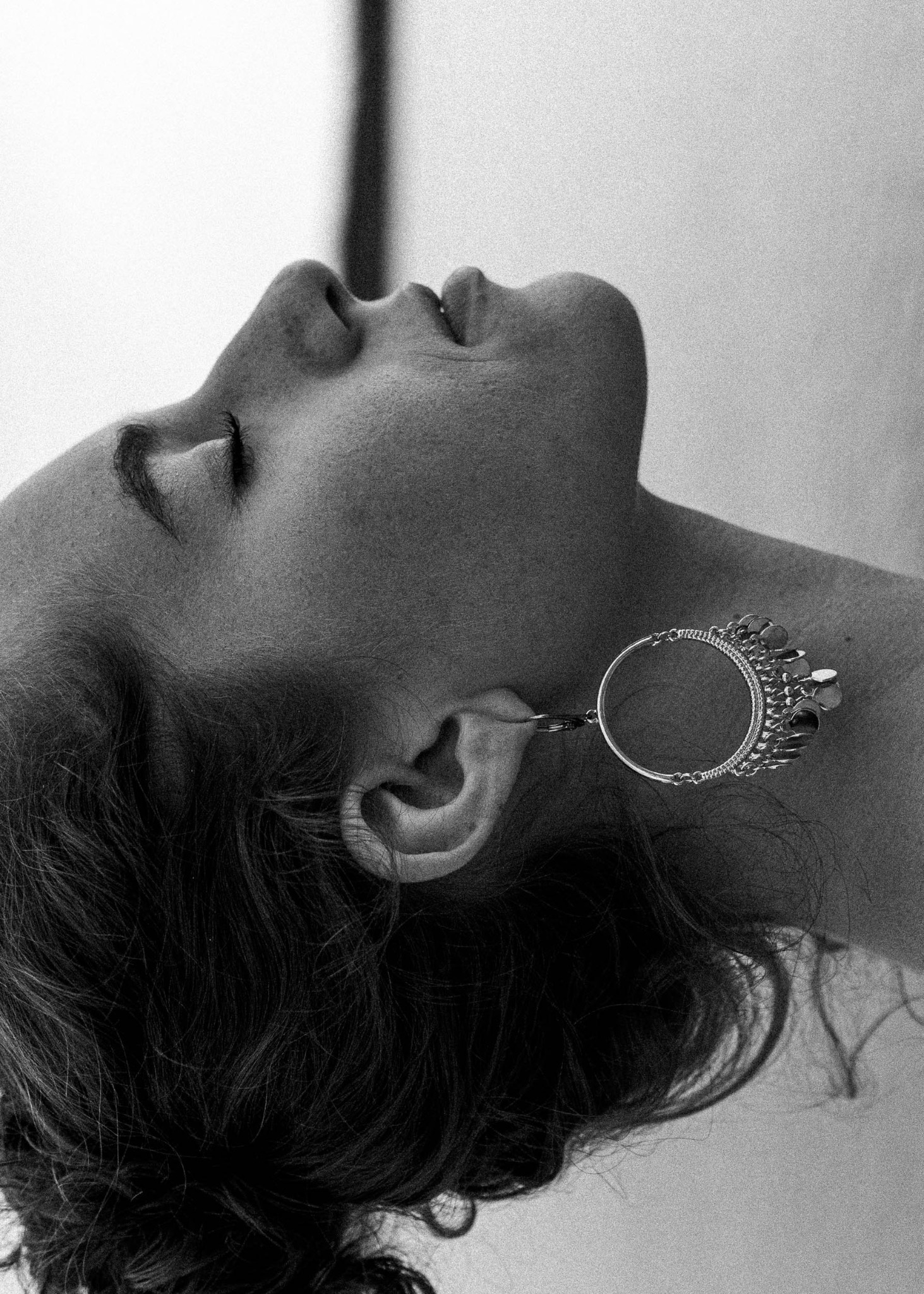 Czarno-białe zbliżenie kobiety z zamkniętymi oczami, odchyloną głową i dużym, okrągłym kolczykiem z ozdobami.