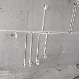 NAZARII HIRNYI - Białe przewody elektryczne zamocowane do surowego, betonowego sufitu i ściany, przygotowane do podłączenia oświetlenia, z pętlami zwisającymi w miejscach przyszłych punktów świetlnych.