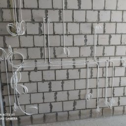 NAZARII HIRNYI - Białe kable elektryczne prowadzone po surowej ścianie z bloczków betonowych, z widocznym planem na kartce przyklejonej do ściany.