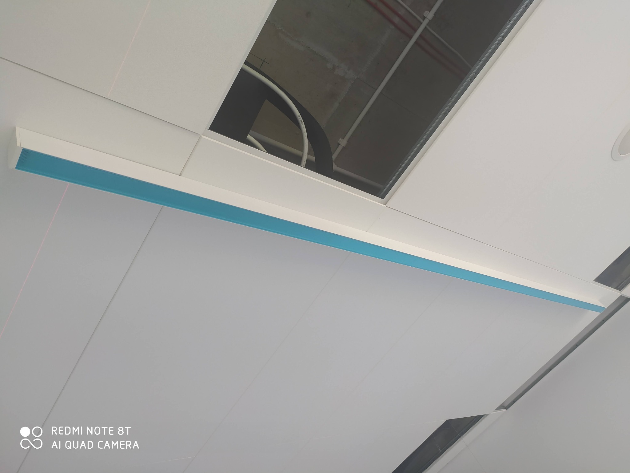 Sufit podwieszany z widoczną linią oświetleniową LED z niebieskim akcentem oraz otwartym modułem sufitowym ukazującym instalacje powyżej.