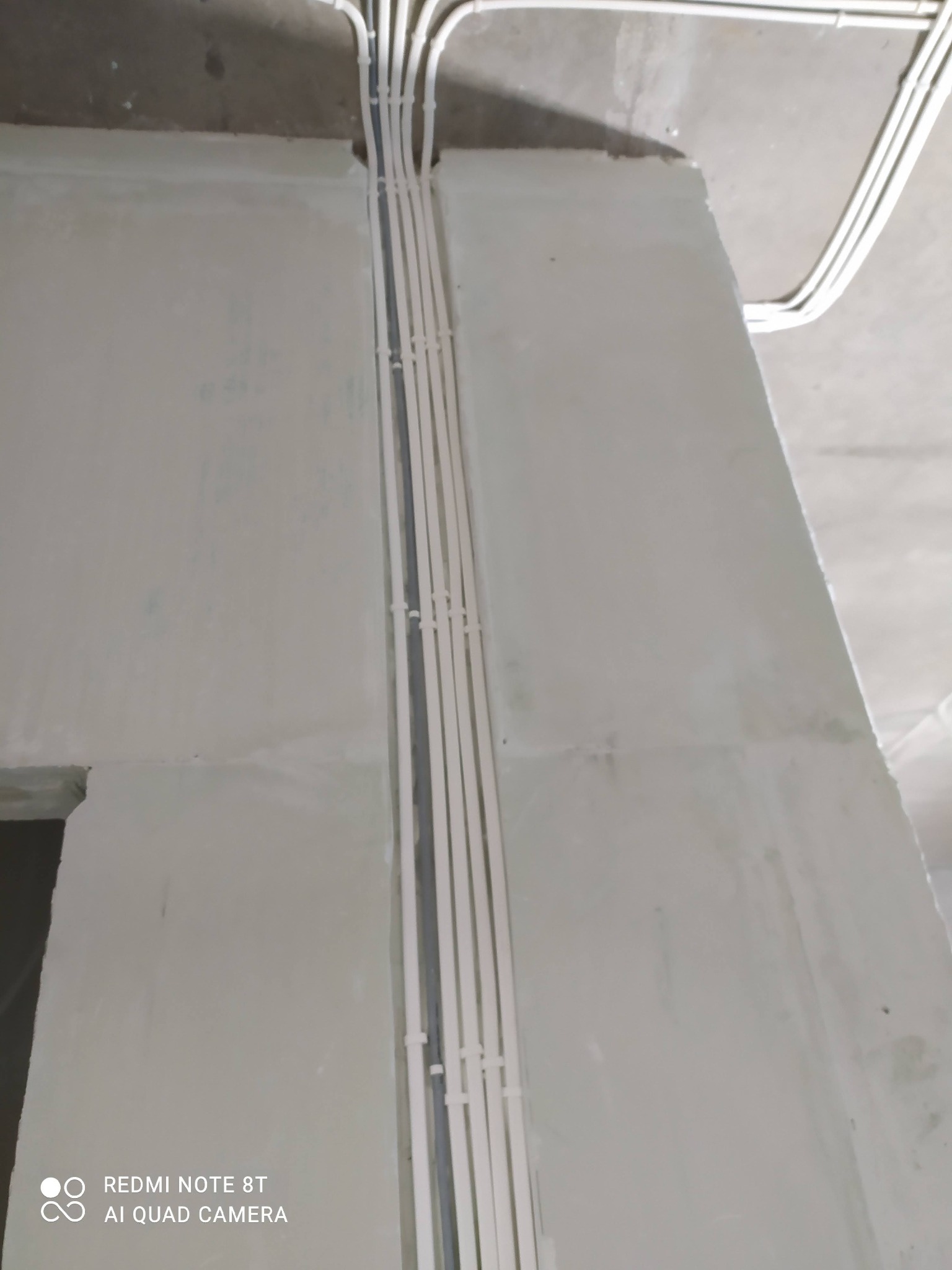 Białe kable elektryczne prowadzone wzdłuż surowej ściany, zabezpieczone plastikowymi opaskami zaciskowymi, widoczne pod sufitem.