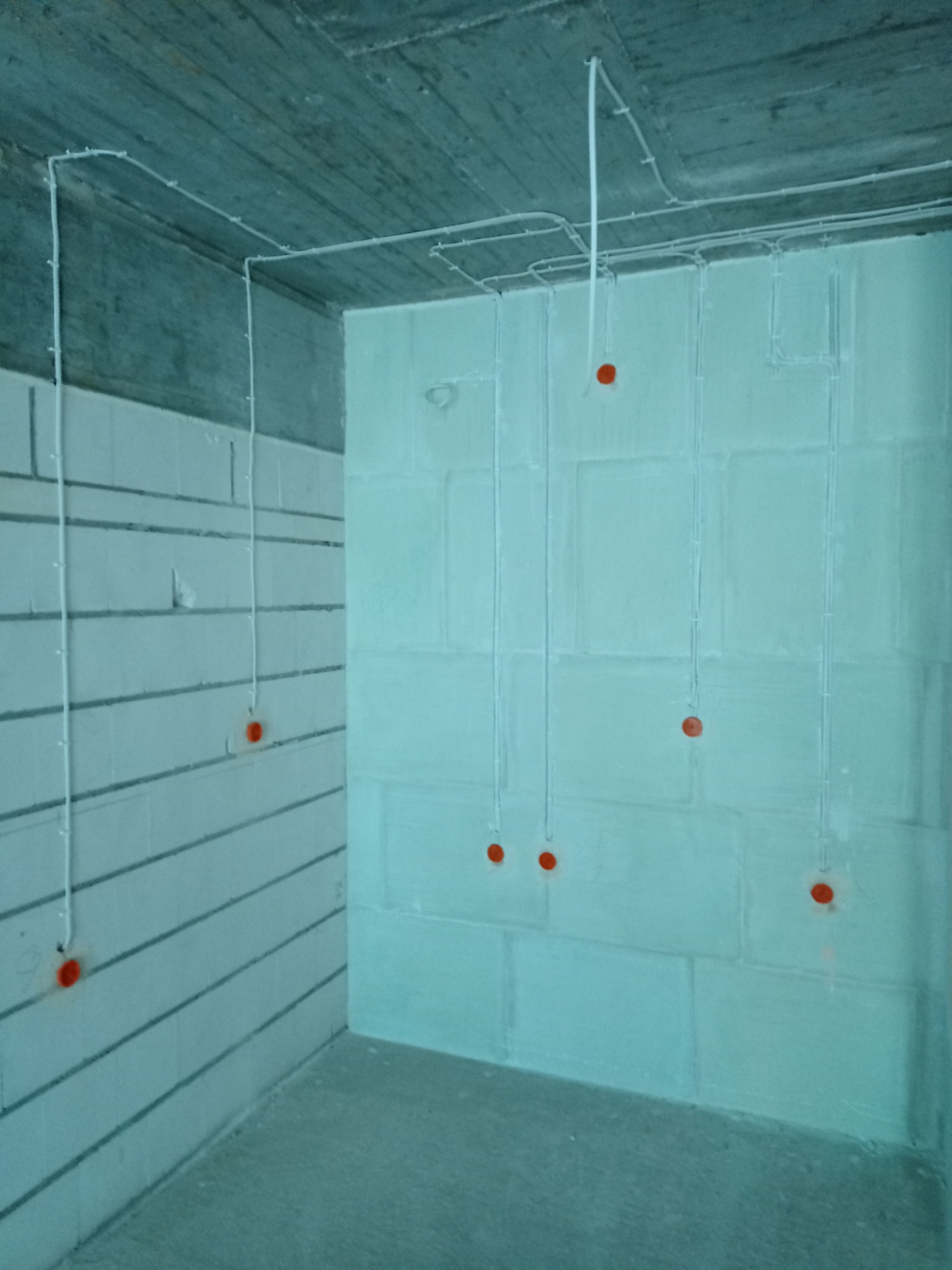 Surowy stan: białe kable elektryczne prowadzone po ścianach z betonu komórkowego i suficie, z widocznymi, pomarańczowymi puszkami pod gniazdka.