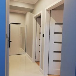 Midgard - Korytarz po remoncie z białymi drzwiami z poziomymi przeszkleniami, jasnymi płytkami na podłodze i szafą z lustrem w tle.