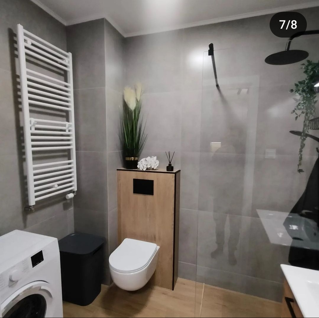 Nowoczesna łazienka w Warszawie z szarymi płytkami, podwieszaną toaletą z drewnianą obudową, grzejnikiem drabinkowym i kabiną prysznicową typu walk-in.